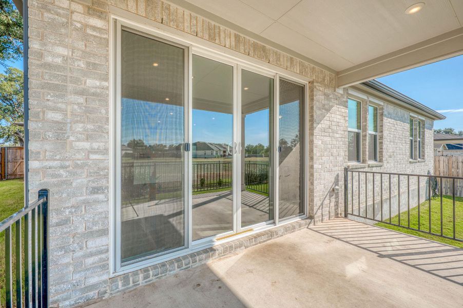 A covered concrete patio sits framed by light brick walls and expansive sliding glass doors.