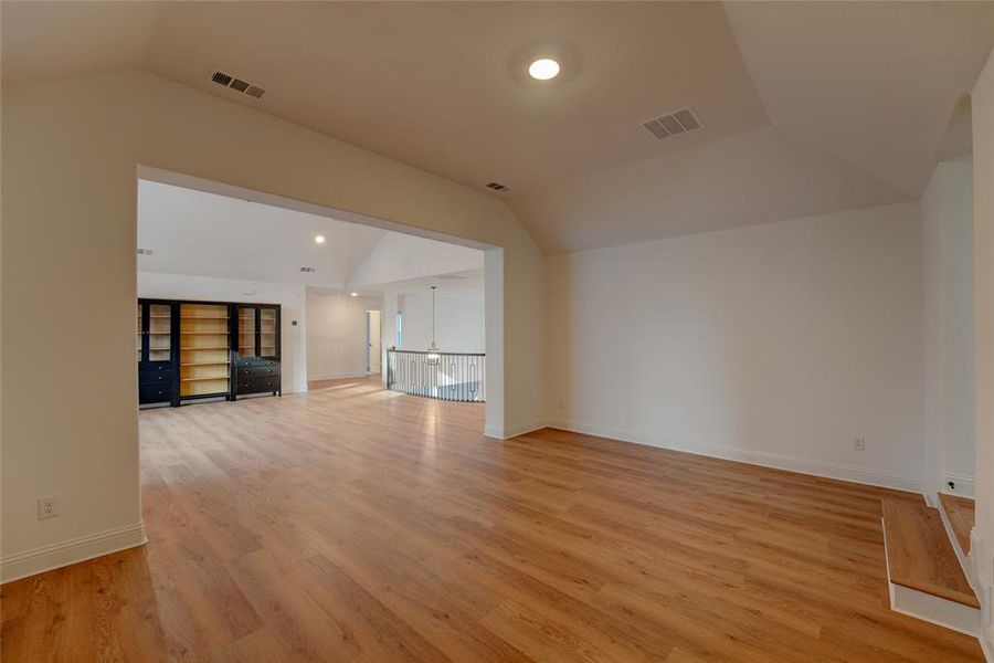 Living room featuring vinyl finished floors, baseboards, visible vents, and vaulted ceiling