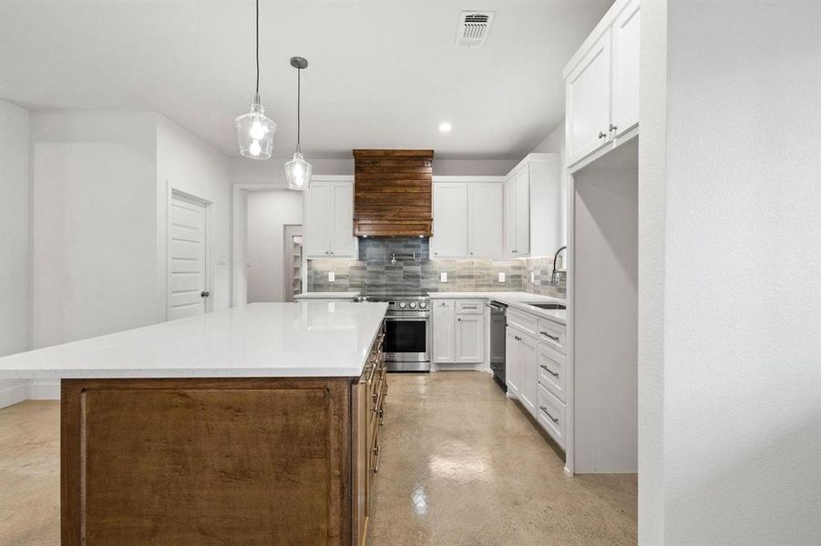 Kitchen with white cabinets, tasteful backsplash, a kitchen island, concrete flooring, and decorative light fixtures