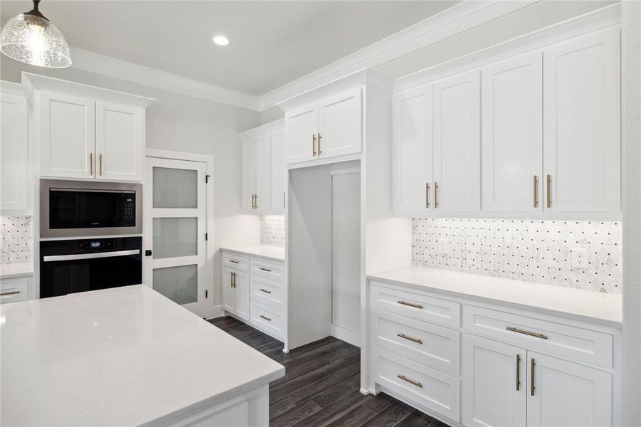 Kitchen featuring stainless steel microwave, white cabinets, backsplash, decorative light fixtures, and oven