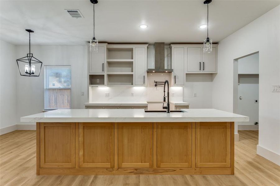 Kitchen featuring hanging light fixtures, light wood finished floors, light stone countertops, wall chimney range hood, and recessed lighting Kitchen featuring hanging light fixtures, light wood finished floors, light stone countertops, wall chimney range hood, and recessed lighting