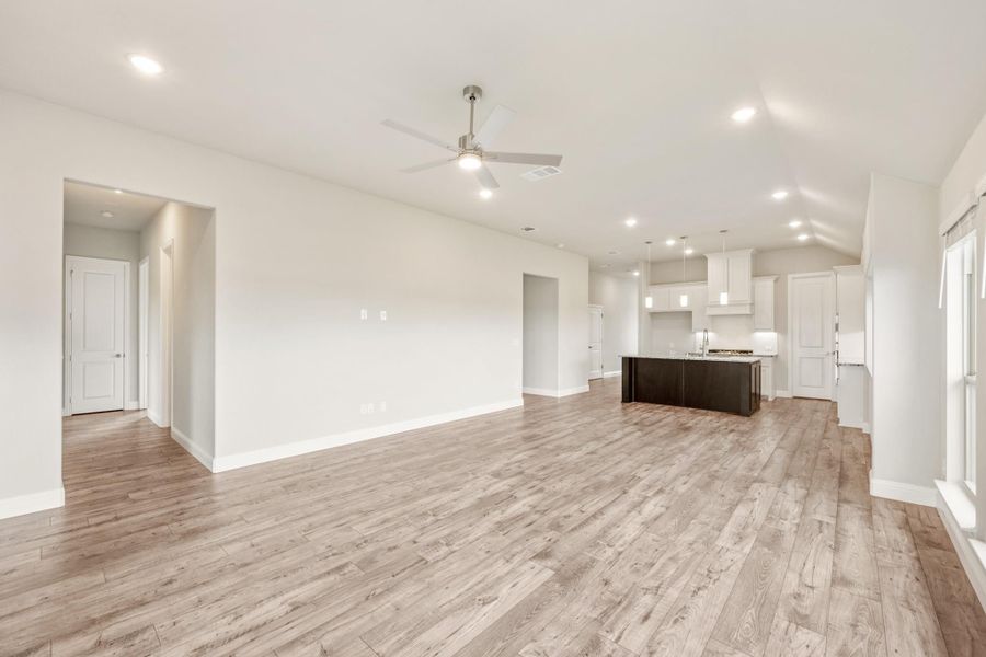 Open living area with light wood floors, ceiling fan, and kitchen island in background Open living area with light wood floors, ceiling fan, and kitchen island in background