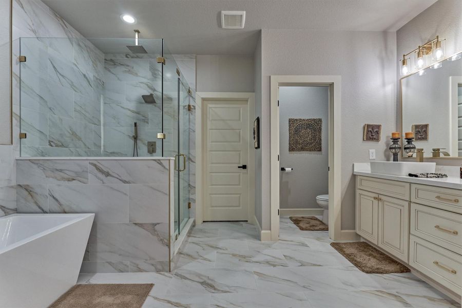 Retreat to a spa-like primary bathroom with a freestaning soaking tub, frameless glass shower and dual vanities surrounded by elegant finishes. Retreat to a spa-like primary bathroom with a freestaning soaking tub, frameless glass shower and dual vanities surrounded by elegant finishes.