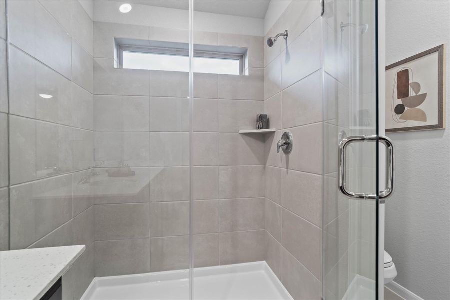 Enjoy a spacious, glass-enclosed shower featuring elegant large-format tile surrounds, sleek chrome fixtures, a built-in shelf, and natural light from a high horizontal window.