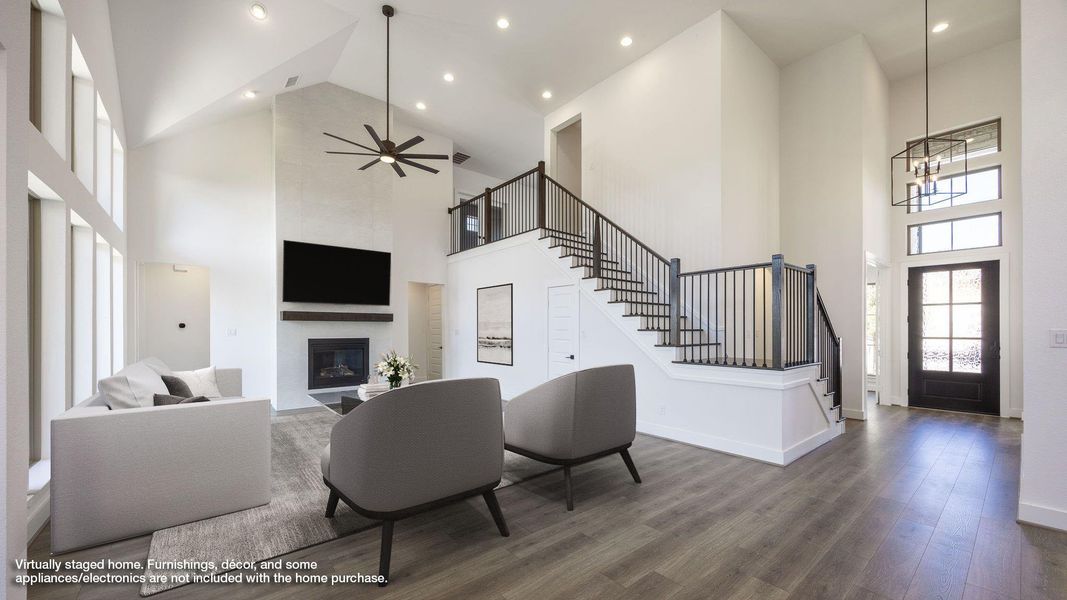 Living area featuring ceiling fan, a fireplace, a high ceiling, wood finished floors, and stairs Living area featuring ceiling fan, a fireplace, a high ceiling, wood finished floors, and stairs
