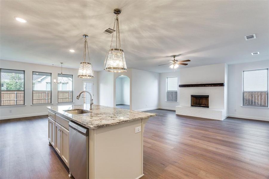 Kitchen with sink, dark hardwood / wood-style floors, stainless steel dishwasher, hanging light fixtures, and an island with sink