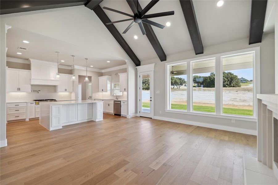 Unfurnished living room with sink, high vaulted ceiling, beamed ceiling, ceiling fan, and light hardwood / wood-style flooring