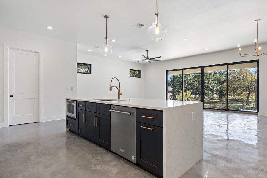 Kitchen featuring finished concrete floors, a ceiling fan, pendant lighting, light stone counters, and dark cabinets Kitchen featuring finished concrete floors, a ceiling fan, pendant lighting, light stone counters, and dark cabinets