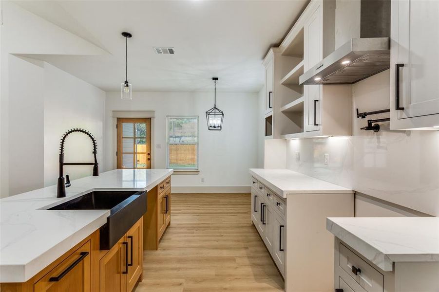 Kitchen with white cabinetry, wall chimney range hood, light stone counters, and light wood-style floors Kitchen with white cabinetry, wall chimney range hood, light stone counters, and light wood-style floors