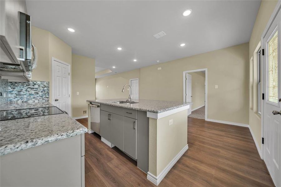 Kitchen with sink, backsplash, stainless steel dishwasher, a kitchen island with sink, and dark wood-type flooring