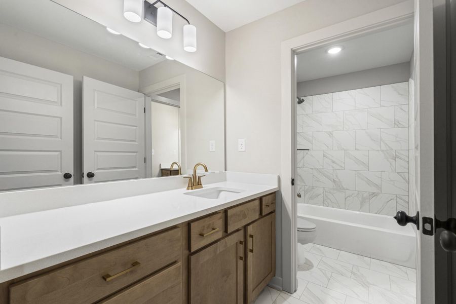Bathroom featuring a single vanity with wood-finish cabinetry, a white countertop, and a brass-tone faucet Bathroom featuring a single vanity with wood-finish cabinetry, a white countertop, and a brass-tone faucet
