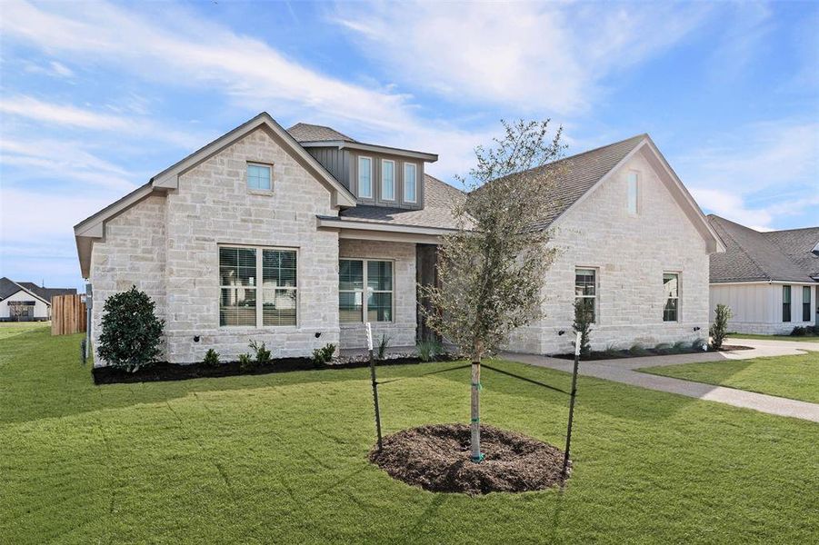 View of front of home featuring stone siding, a front yard, and roof with shingles