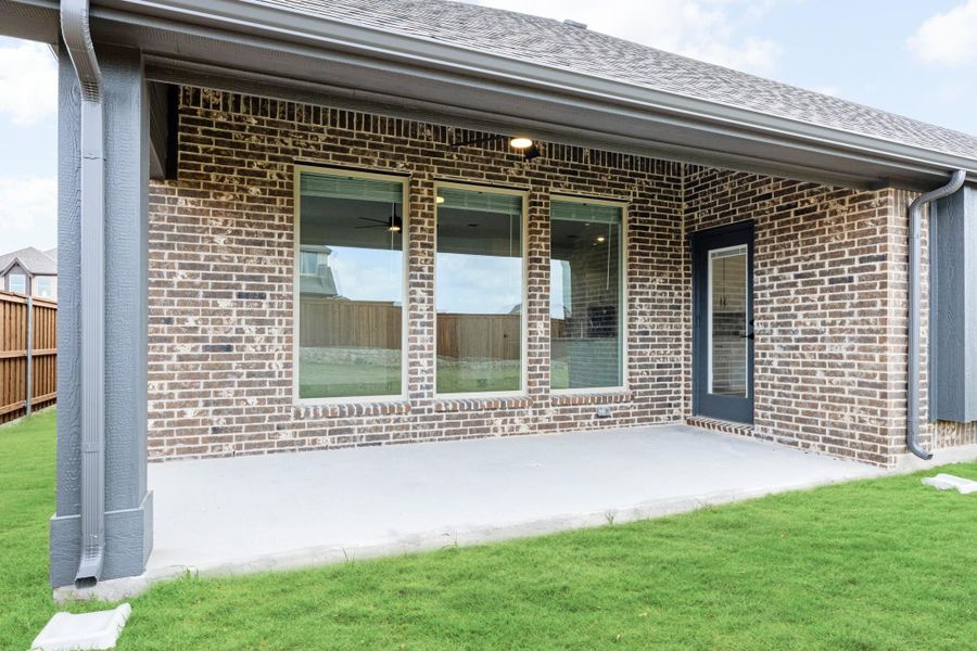 Covered back patio with concrete slab, brick exterior, large windows, and green lawn
