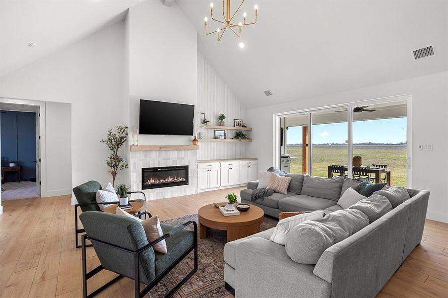 Living room featuring high vaulted ceiling, ceiling fan with notable chandelier, light hardwood / wood-style flooring, beam ceiling, and a tiled fireplace