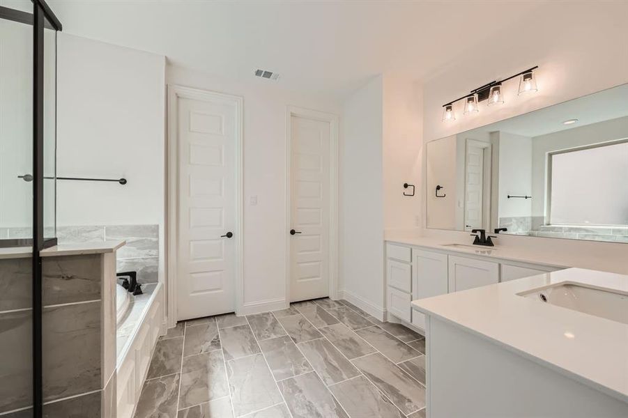 Primary bathroom featuring tile patterned floors, vanity, and tiled bath