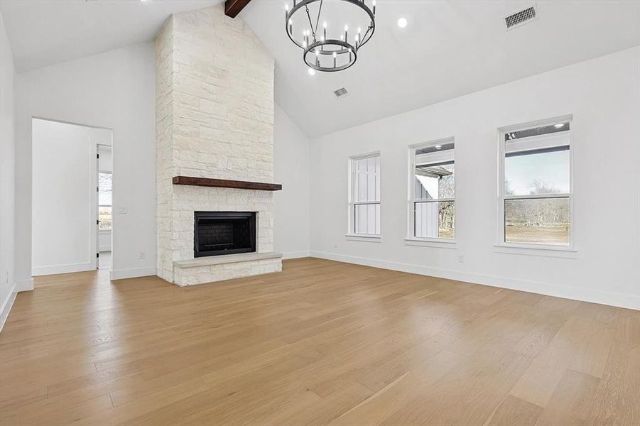 Unfurnished living room with beam ceiling, high vaulted ceiling, a stone fireplace, and light wood-type flooring