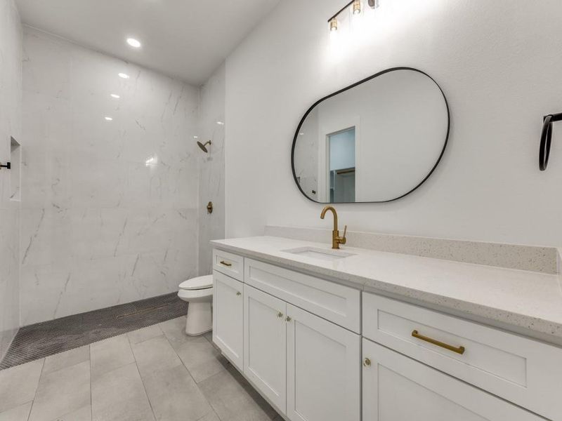 Bathroom with toilet, vanity, tile patterned flooring, and tiled shower