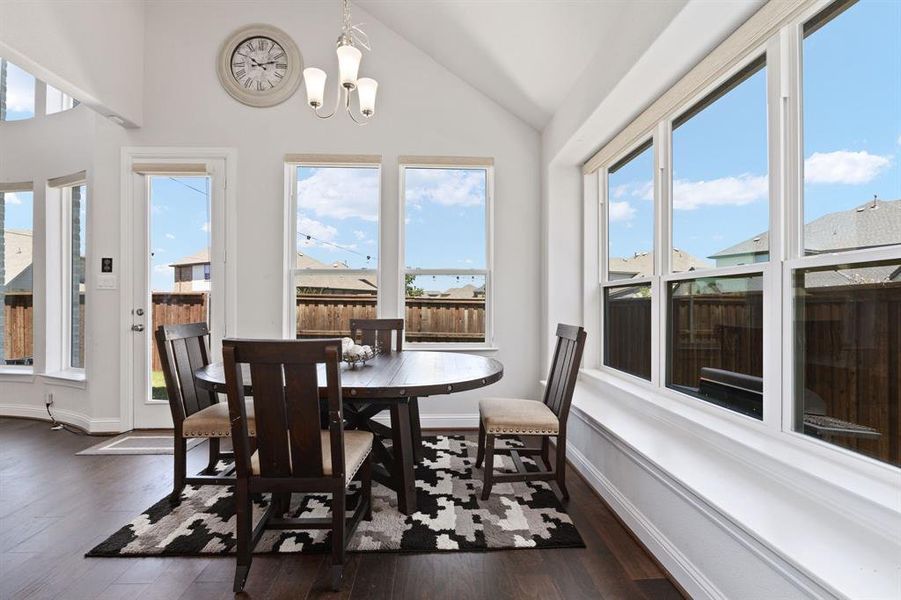 Dining room with a healthy amount of sunlight, vaulted ceiling, dark wood-type flooring, and a notable chandelier