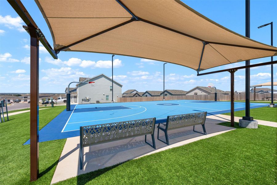 A shaded seating area overlooks the neighborhood basketball court under sunny blue skies. A shaded seating area overlooks the neighborhood basketball court under sunny blue skies.