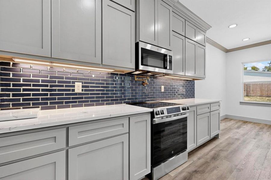Kitchen featuring stainless steel appliances, ornamental molding, light stone countertops, decorative backsplash, and light wood finished floors