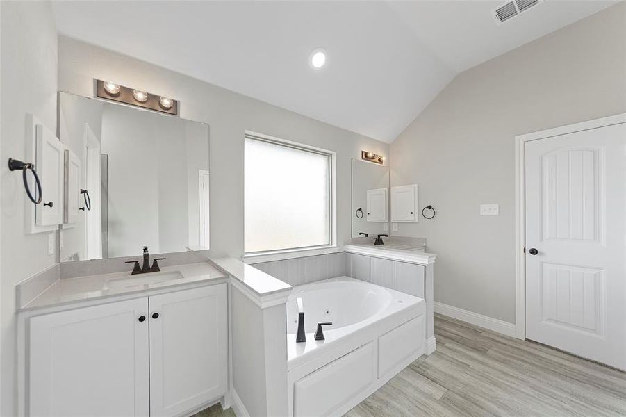 Bathroom featuring a bathtub, vanity, vaulted ceiling, and hardwood / wood-style flooring