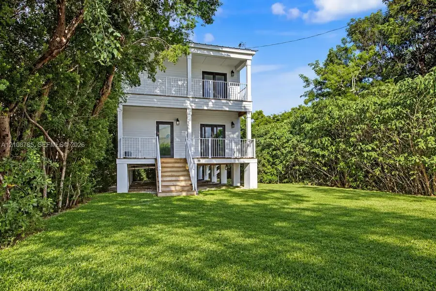 Two-story home with white horizontal siding, elevated foundation, stacked porches with metal railings, and exterior staircase Two-story home with white horizontal siding, elevated foundation, stacked porches with metal railings, and exterior staircase