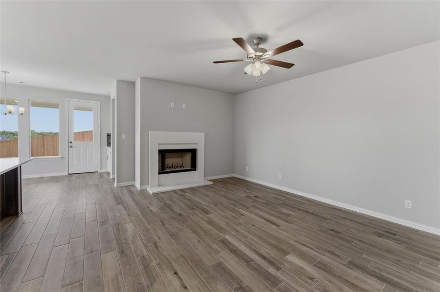 Spacious living area featuring wood-finish flooring, a contemporary fireplace with a white mantel, and a ceiling fan with integrated lighting