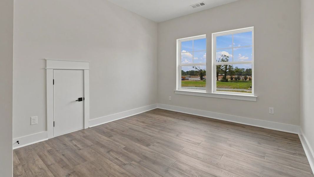 Upstairs bedroom with elevated wood flooring and two windows.