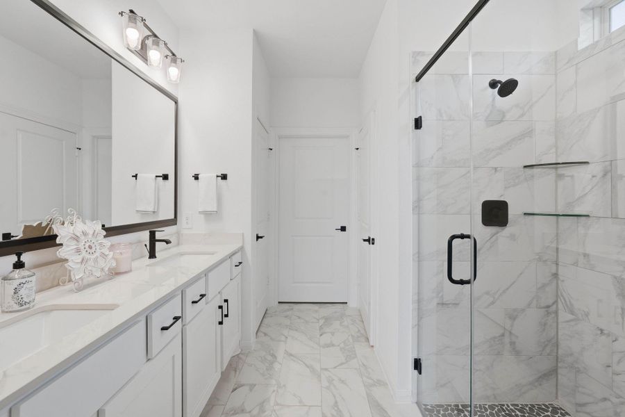 The primary bathroom impresses with a glass-enclosed shower, marble-style finishes, and a double vanity that blends function with elegance.