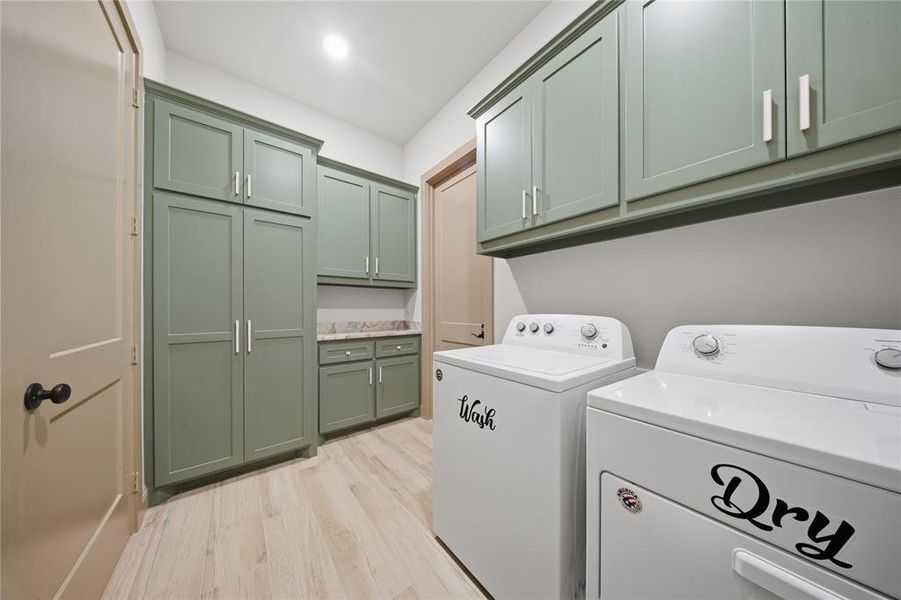 Dedicated laundry area featuring sage green cabinetry, a built-in countertop, and wood-finish flooring