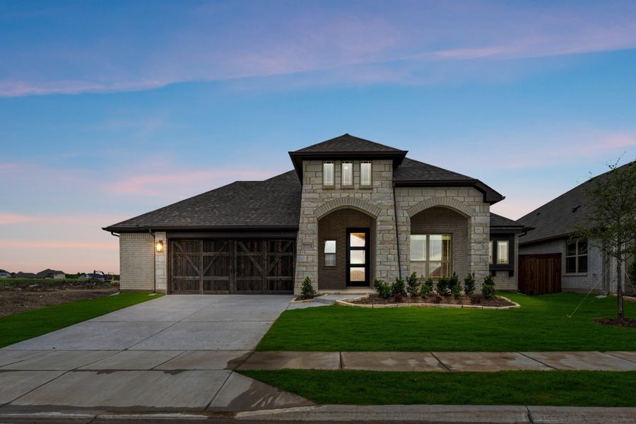 Single-story home with stone and brick exterior, wood garage doors, arched entry, and manicured front lawn at dusk Single-story home with stone and brick exterior, wood garage doors, arched entry, and manicured front lawn at dusk
