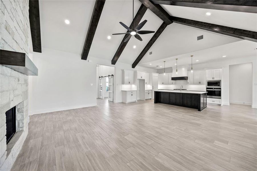 Unfurnished living room with a barn door, a fireplace, ceiling fan, high vaulted ceiling, and light wood-style flooring Unfurnished living room with a barn door, a fireplace, ceiling fan, high vaulted ceiling, and light wood-style flooring