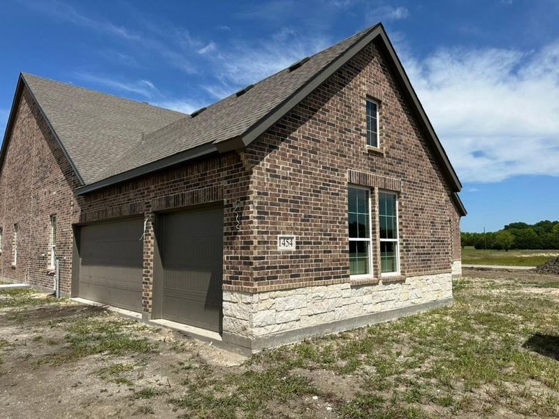 Brick exterior featuring a stone accent foundation, multiple windows, and a two-car garage