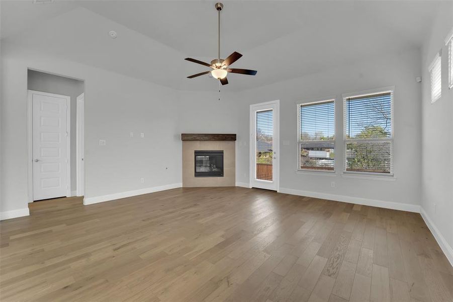 Unfurnished living room with a tiled fireplace, light wood-style flooring, and ceiling fan