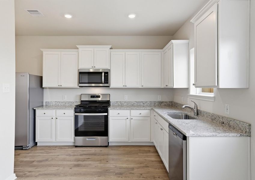 Kitchen featuring an undermount sink beneath a window, granite countertops, and white cabinetry.