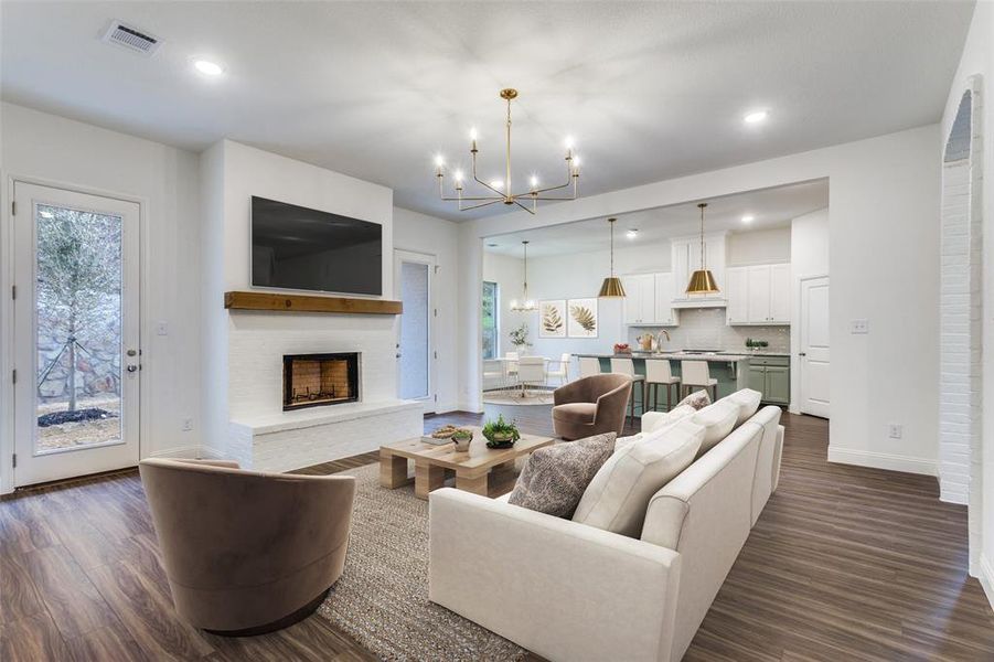 Living area with dark wood-style flooring, visible vents, baseboards, a fireplace with raised hearth, and a chandelier