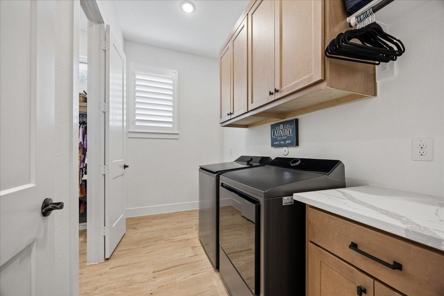 Functional laundry room featuring durable wood-plank tile flooring, overhead custom soft close cabinets, and built-in side soft close cabinetry with additional granite countertop space. This room is designed for convenience and accommodates full-sized appliances.