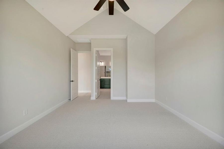 Spacious room featuring vaulted ceilings, light-toned carpeting, and a dark-finished ceiling fan