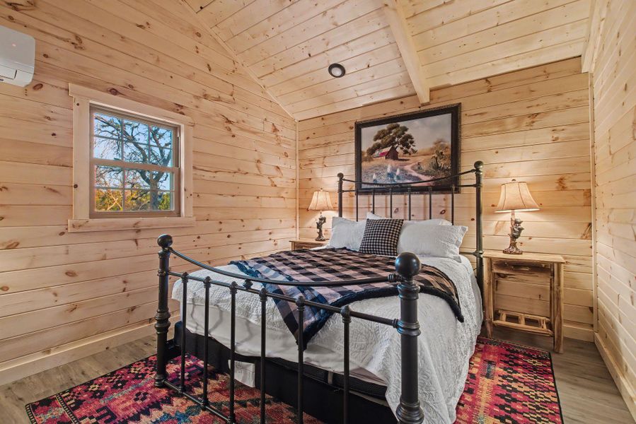 Bedroom with wood walls, vaulted ceiling, wood finished floors, wood ceiling, and a wall unit AC