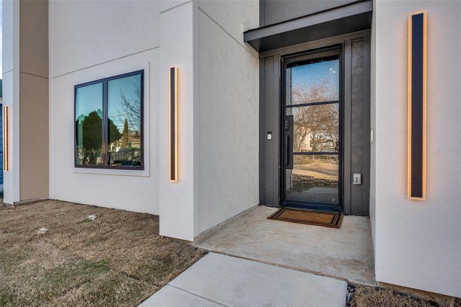 Contemporary entry featuring a black-framed glass door, concrete porch, and modern vertical exterior lighting fixtures