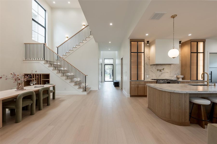 A long interior sightline reveals the home’s scale and flow, with the two story dining room, custom white oak staircase and chef’s kitchen unfolding seamlessly toward the great room beyond. A long interior sightline reveals the home’s scale and flow, with the two story dining room, custom white oak staircase and chef’s kitchen unfolding seamlessly toward the great room beyond.