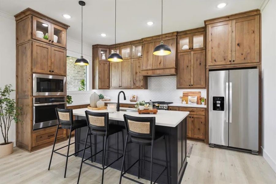 Kitchen featuring stainless steel appliances, glass fronted cabinets, a kitchen breakfast bar, light wood-style floors, and a center island with sink