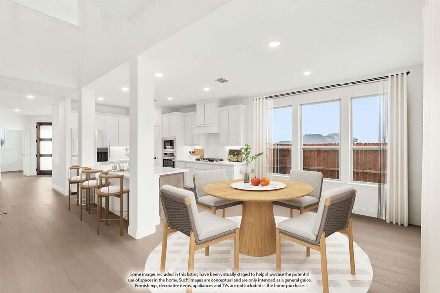Open-plan dining area with round wood table and white kitchen with island in background, hardwood floors throughout Open-plan dining area with round wood table and white kitchen with island in background, hardwood floors throughout