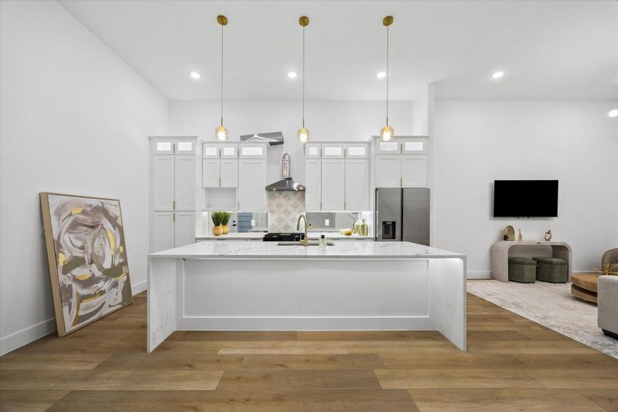 This modern kitchen features sleek white cabinetry, a large marble island with a waterfall edge, and stylish pendant lighting. The open layout flows into a cozy living area with a mounted TV, perfect for entertaining. This modern kitchen features sleek white cabinetry, a large marble island with a waterfall edge, and stylish pendant lighting. The open layout flows into a cozy living area with a mounted TV, perfect for entertaining.