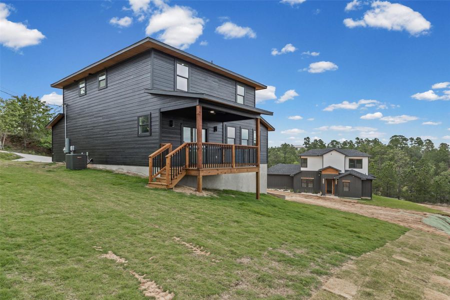 Modern two-story residence featuring dark horizontal siding and a covered deck with natural wood railings Modern two-story residence featuring dark horizontal siding and a covered deck with natural wood railings