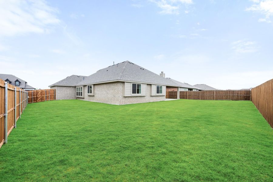 Large backyard with green lawn, wood privacy fence, and brick home with gray shingle roof visible in background