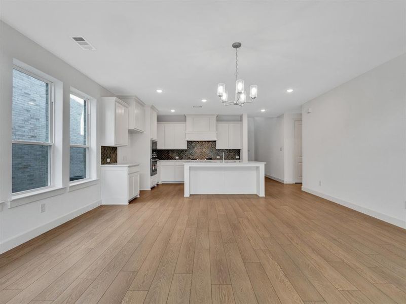 Kitchen featuring white cabinetry, a notable chandelier, a center island, light hardwood / wood-style floors, and decorative backsplash