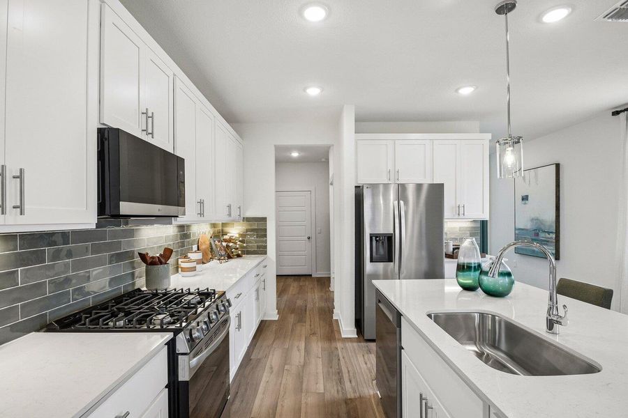 A well-appointed kitchen features stainless steel appliances, pristine white cabinetry, and durable wood flooring.