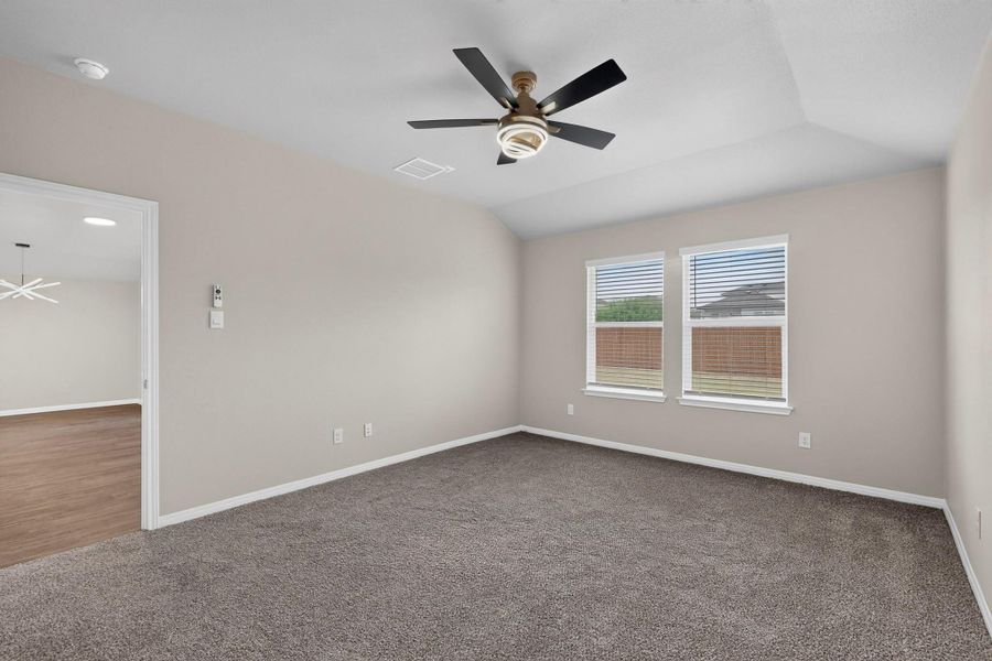 Plush carpeting anchors this spacious bedroom featuring a high vaulted ceiling and dual windows.