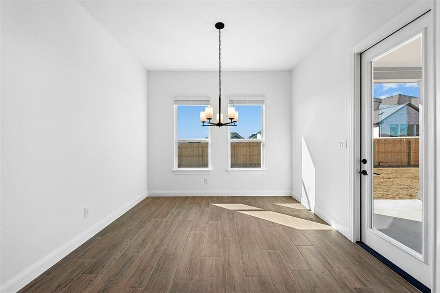 Spacious room featuring wood-finish flooring, two large windows, a contemporary chandelier, and a full-light exterior door